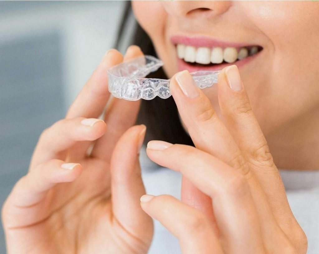 Woman holding clear Invisalign aligner for teeth straightening