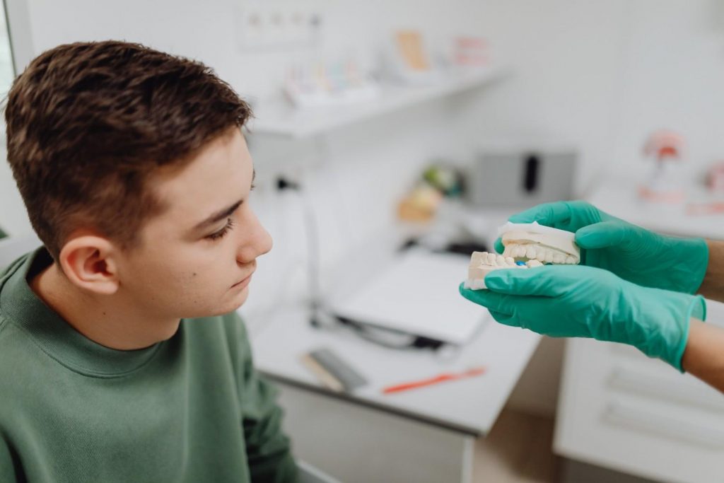 Teenager attending a dental consultation, examining a dental model held by a dentist