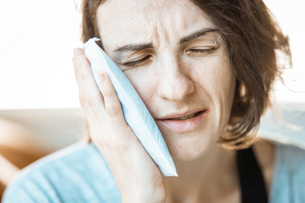 A woman in discomfort applying a cold compress to her cheek